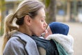 Sideview of a late-term mother in her 40s lovingly holding her newborn baby in a baby carrier and kissing him gently Royalty Free Stock Photo