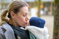 Sideview of a late-term mother in her 40s lovingly holding her newborn baby in a baby carrier and kissing him gently Royalty Free Stock Photo