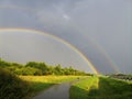 Sidewalk near highway. Rainbow in gray sky.