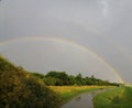 Sidewalk near highway. Rainbow in gray sky.