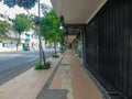 A sidewalk for pedestrians with a few trees, shophouses that are closed and the black door and the main road beside it Royalty Free Stock Photo