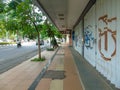 A sidewalk for pedestrians with a few trees, shophouses that are closed and the door gets vandalism and the main road beside it Royalty Free Stock Photo