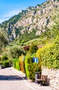 Sideway of a road with wooden bench, dead end road sign, shaped hedge on stone fence and private houses, hotels of a beautiful