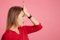 Sideways portrait of forgetful woman remembers something important, keeps hand on forehead, poses against pink background with cop