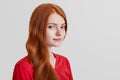 Sideways portrait of freckled serious red haired female model looks confidently into camera, poses against white background with c Royalty Free Stock Photo
