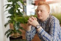 A sideways portrait of handsome young freckled man with stylish red hair dressed in checked shirt sitting near green palm tree hol Royalty Free Stock Photo