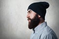 A sideways portrait of stylish bearded man wearing checked shirt and black cap having tatoo on his neck looking into distance whil Royalty Free Stock Photo