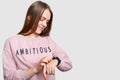 Sideways shot of attractive female checks time on wrist watch, wears casual jumper, waits for someone, makes appointment, has long Royalty Free Stock Photo