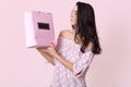 Sideways shot of brunette serious young woman looks at gift bag, wears fashionable summer dress, enjoys recieving present, poses