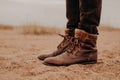 Sideways shot of man in shaggy brown shoes on lay surface. Pair of boots on sand. Male has outdoor walk in old footwear