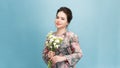 Sideways shot of pleased attractive young woman holds spring flowers, poses over pink background, has friendly smile on face, has