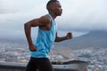 Sideways shot of sporty dark skinned runner wears blue vest, participates in triathlon race, has fitness lifestyle