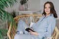 Sideways shot of young female reader hold book in hands, rests at home, wears pyjamas, enjoys calm atmosphere, reading bestseller,