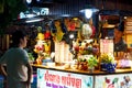 A man stands near an Asian stall with desserts and drinks in the evening