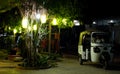 Small Asian taxi stands near a tree decorated with decorative lights. Small lit courtyard