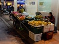 Young Asian girl seller of bananas on the street of the night city looks into the smartphone