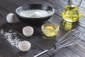 Sieve on black bowl with flour. Glass bottle with oil, eggs, eggshell, broken egg in plate, metal whisk, wooden spoon with flour Royalty Free Stock Photo