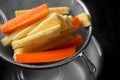 Sieve with cut parsnips and carrots over pot of water, closeup