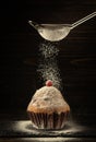 From the sieve, powdered sugar is sprinkled onto a baked red berry muffin. Delicious dessert concept on black background