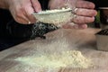 sieving flour at table against black background