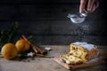 Sieving powdered sugar on a christmas cake, in germany christstollen, orange and spices blurred in the back on a rustic wooden ta