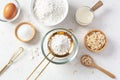 Sifting flour with gold sieve in glass bowl with baking ingredients on marble kitchen table