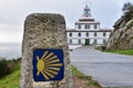 Sign of the Camino de Santiago and Finisterre Lighthouse in the background. In the light of day, in a sky with clouds. Galicia,