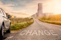 Sign change and car parked off small narrow country road leading to a modern town with tall office and residential building in the