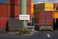 A sign `Einfahrt` entrance` beside the back of a truck entering a container terminal with stacked containers