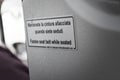 Sign in english and italian in the cabin of an airplane, assking to fasten seat belt when seated Royalty Free Stock Photo