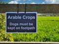 A sign fixed to a wooden stile advises that the field ahead contains arable crops and that dogs must be kept on the footpath