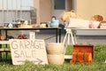 Sign Garage sale written on cardboard near tables with different stuff in yard Royalty Free Stock Photo