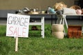 Sign Garage sale written on cardboard near tables with different stuff in yard Royalty Free Stock Photo