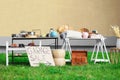 Sign Garage sale written on cardboard near tables with different stuff in yard Royalty Free Stock Photo
