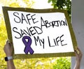 Sign with glitter edge reads Safe Abortion Saved My Live - blurred outdoor background at Reproductive Justice Rally