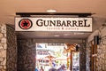 Sign for Gunbarrel Tavern and Eatery with people ourdoors dining on patio through rock door -