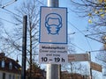 A sign hanging on a pole informing about a zone with the obligation to cover the mouth and nose