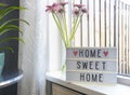 Sign Home sweet home text on lightbox ,windowsill near window with pink flowers, decorative frame modern interior Royalty Free Stock Photo