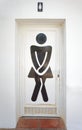 Sign on ladies toilet door, showing person in a dress, needing to pee.