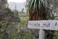 A timber sign in wilderness with the text 'private hut' directing to hidden accommodation in the bush
