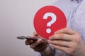 Sign of the question mark made of red paper and smartphone in the hands of a man Royalty Free Stock Photo
