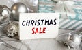 A sign that reads CHRISTMAS SALE stands on the table with gift boxes in the background. Christmas background with decorations from Royalty Free Stock Photo