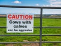 A sign with red and black lettering fixed to a gate to a farm field