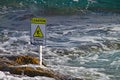 Sign on the rocks in the sea giving the obvious warning of slippery surface