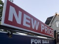 Sign for sale new price by detached house in residential area. Real estate market volatility concept.