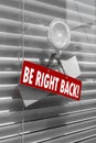 A sign saying `be right back` on a glass door with a white, closed venetian blind