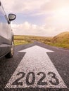 Sign 2023 on small asphalt country road and a side of a car and arrow. Travel and explore concept. Warm sunny day, sun flare. Royalty Free Stock Photo