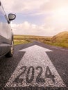 Sign 2024 on small asphalt country road and a side of a car and arrow. Travel and explore concept. Warm sunny day, sun flare. Royalty Free Stock Photo