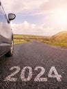 Sign 2024 on a small asphalt road and a side of a car, cloudy sky and country side in the background. Vertical image Royalty Free Stock Photo