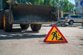 Sign, the symbol of road works is installed on the background of a tractor, a bulldozer with a raised bucket